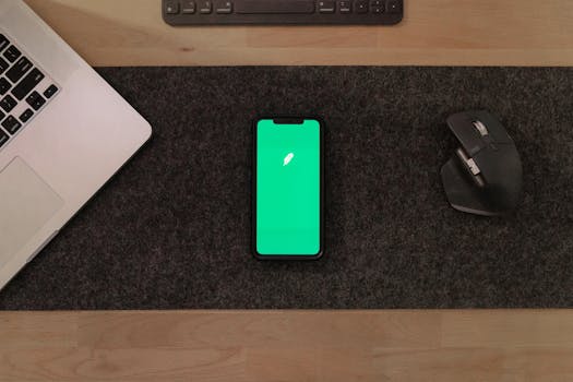 Modern workspace with smartphone, laptop, and mouse on wooden desk.